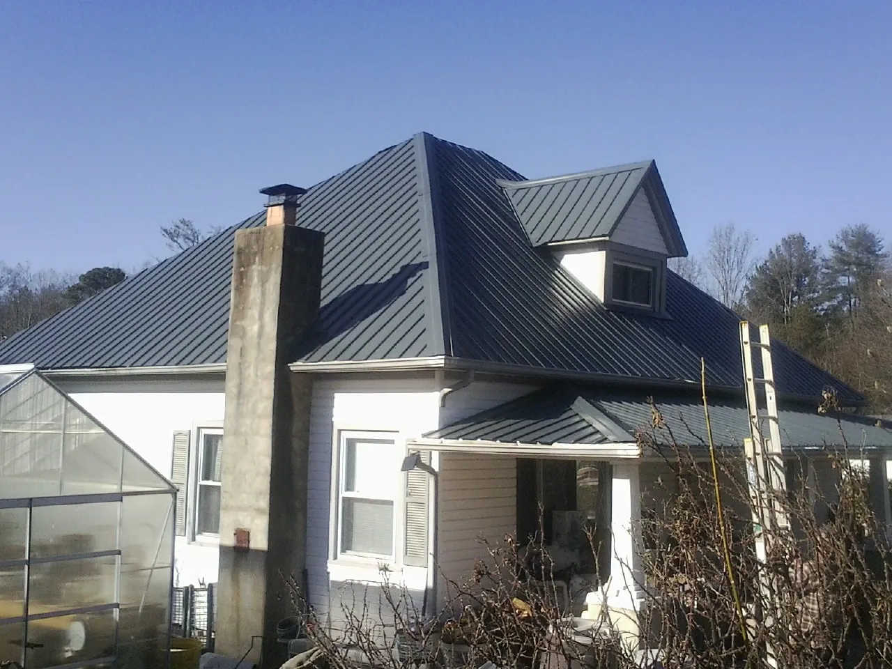 Dark blue standing seam metal roof on a white farmhouse with dormer — Slate & Tile Roof Repair by Roofing Brothers in Norwood