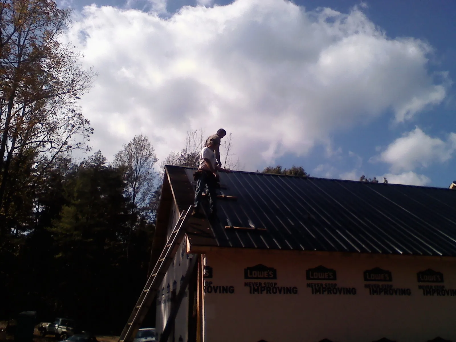 Roofer fastening dark metal panels high against a cloudy sky in Norwood