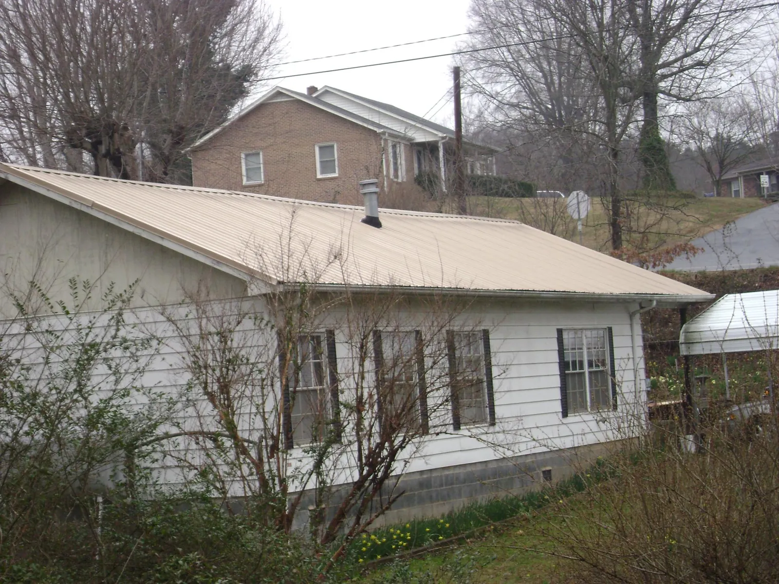 Tan metal roof on a white sided house set into a hillside — Commercial Roofing by Roofing Brothers in Norwood