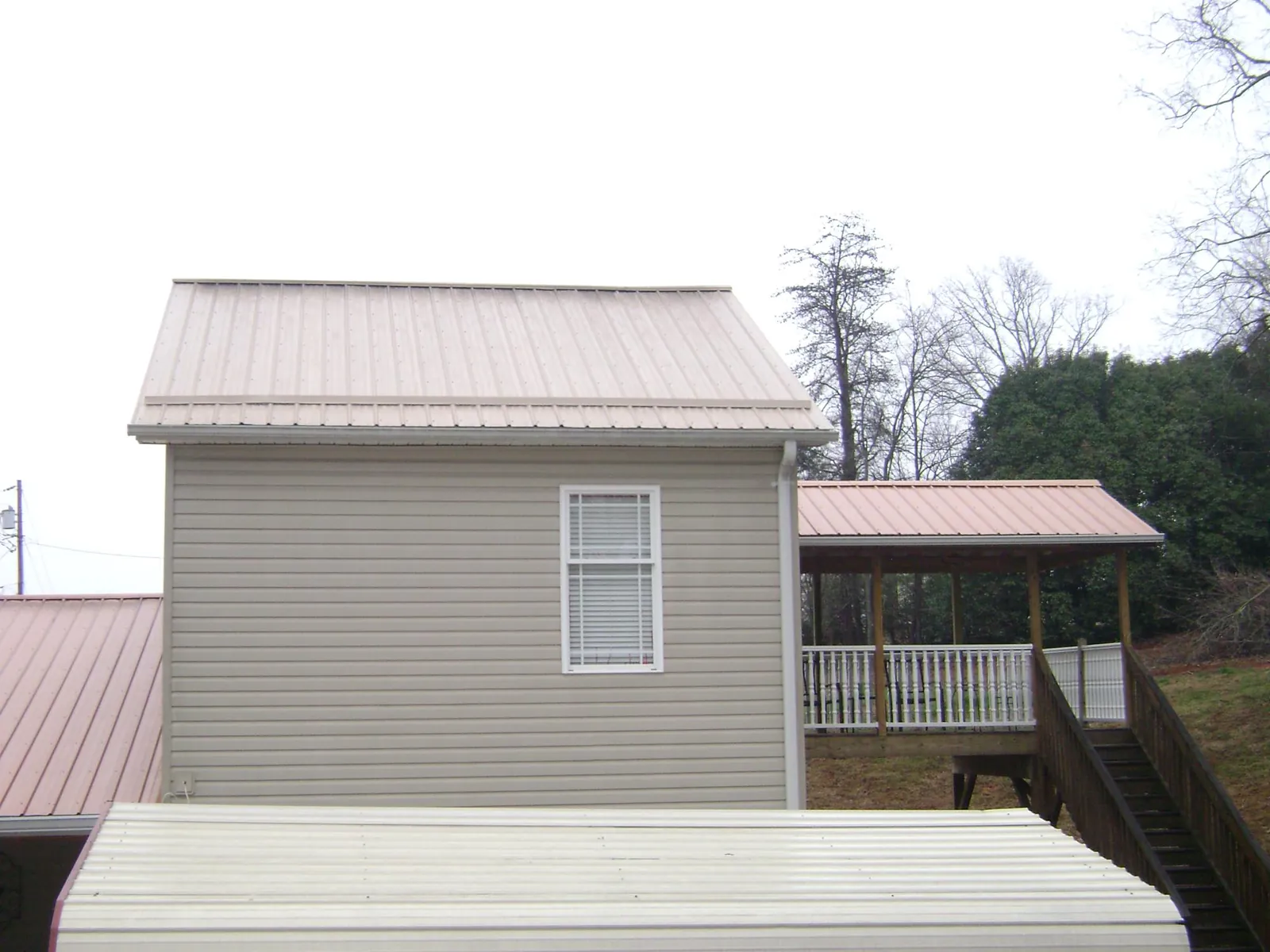 Tan metal roofs on a two story addition and attached porch, from a Roof Replacement job in Norwood